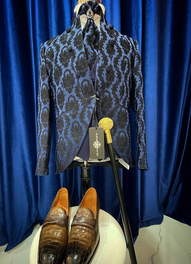 Conjunto de ceremonia azul en maniquí con corbatón, broche, bastón y zapatos