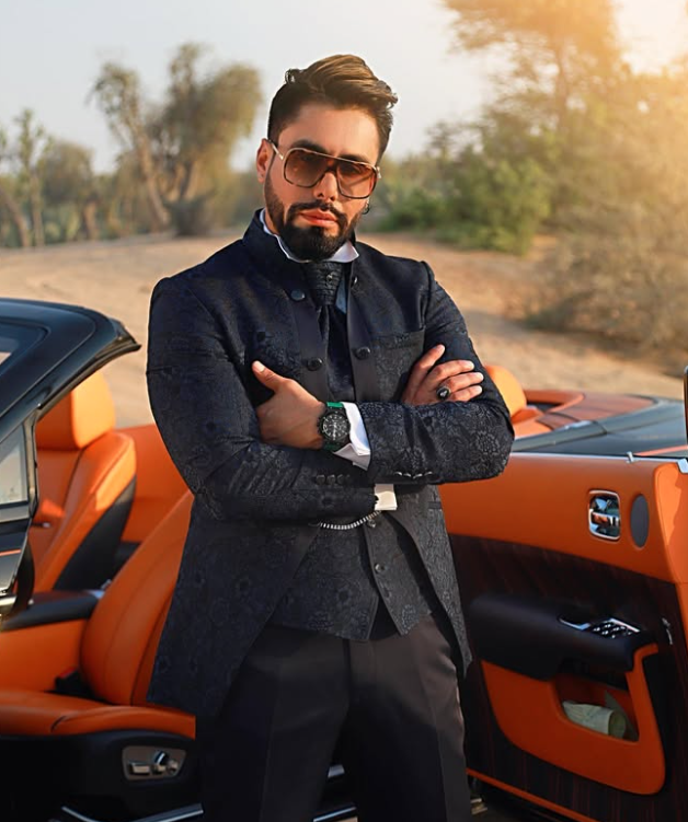 Modelo con traje oscuro de jacquard y gafas junto a un automóvil descapotable