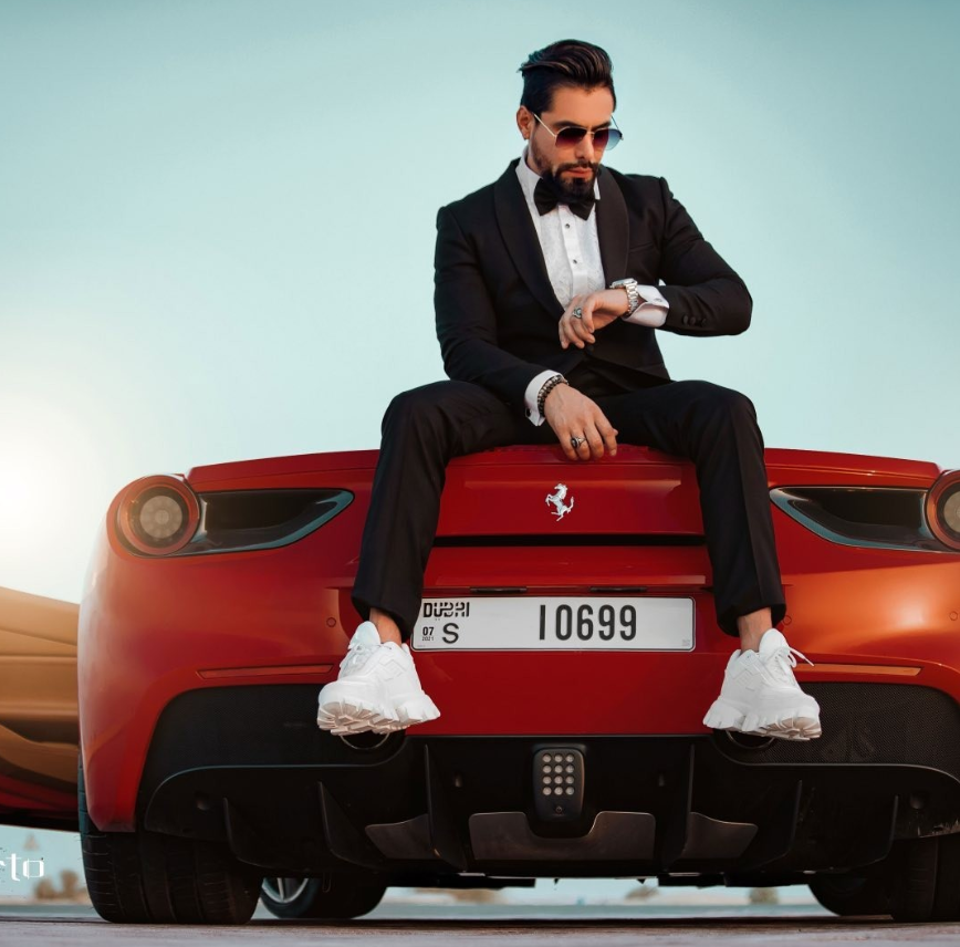 Modelo con esmoquin negro y zapatillas blancas sentado en un auto rojo